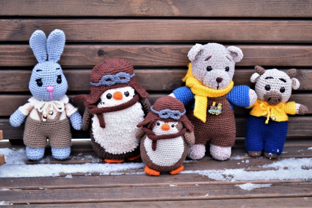 A charming collection of handmade crochet toys on a wooden bench in winter, showcasing unique designs.