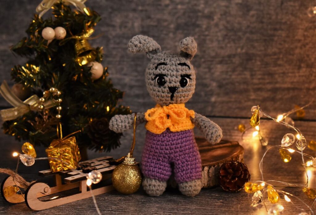 A charming handmade crochet bunny toy surrounded by festive Christmas decorations and lights.