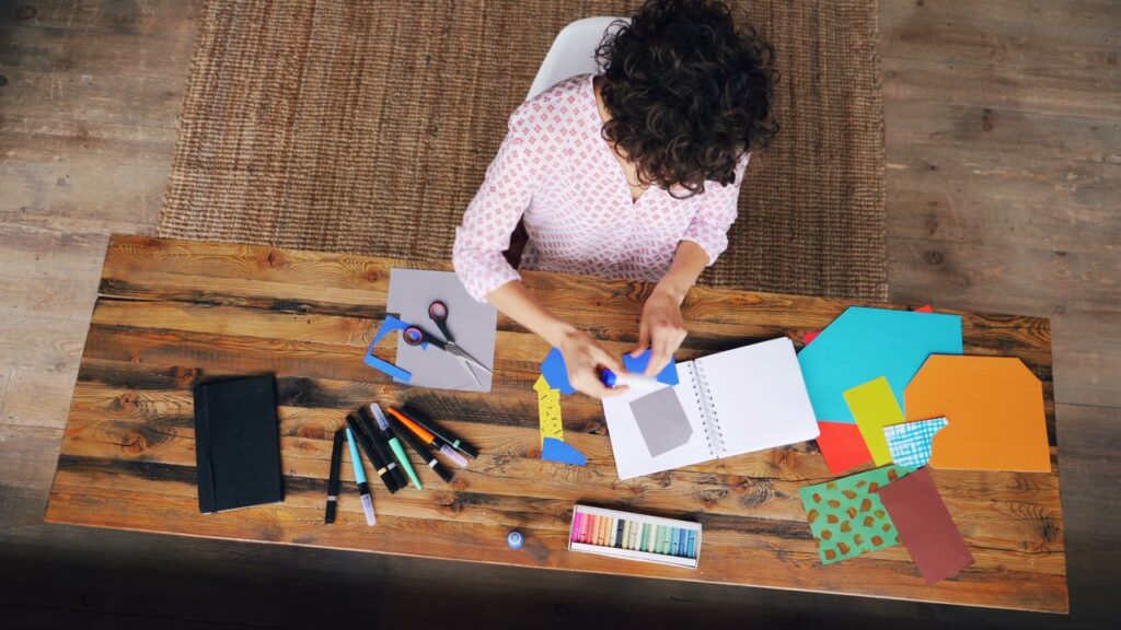 Top view of a woman engaging in paper craft activities at home, using colorful supplies.
