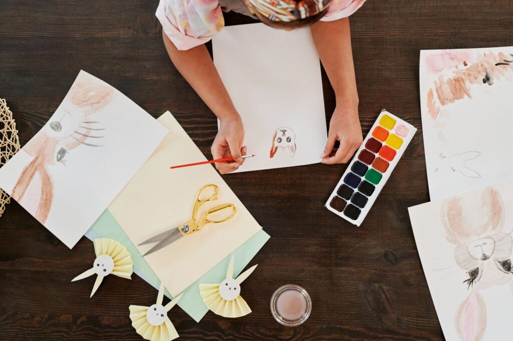 Overhead view of a person painting and crafting with watercolors, surrounded by art supplies.