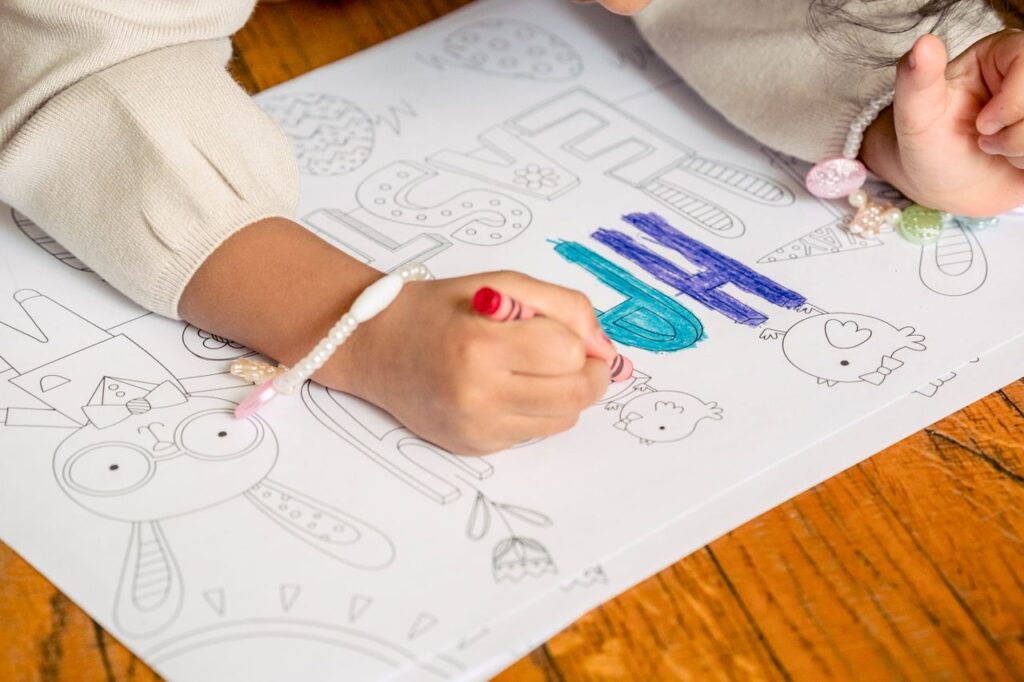 From above of crop unrecognizable little girl drawing in coloring book at home in daytime